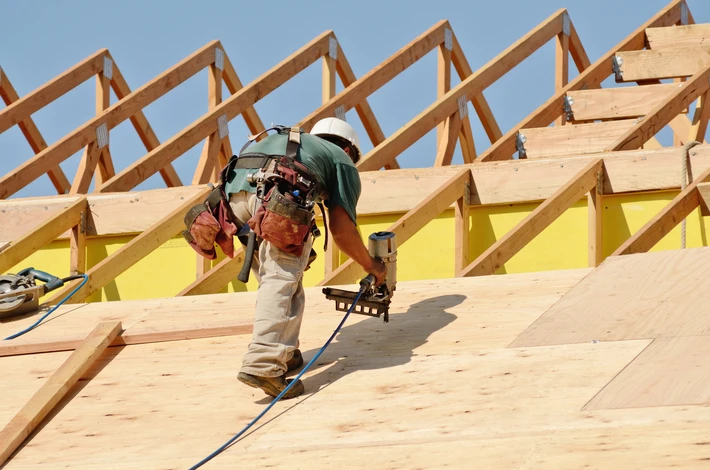 Chantier de construction extérieur avec charpentier installant une toiture