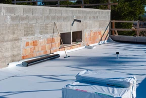 Chantier de construction extérieur avec ouvriers installant une membrane d'étanchéité blanche sur toiture terrasse