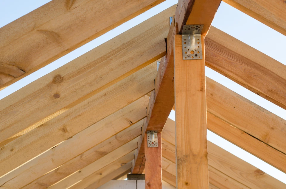Chantier de construction extérieur avec charpente en bois massif sous ciel bleu nuageux